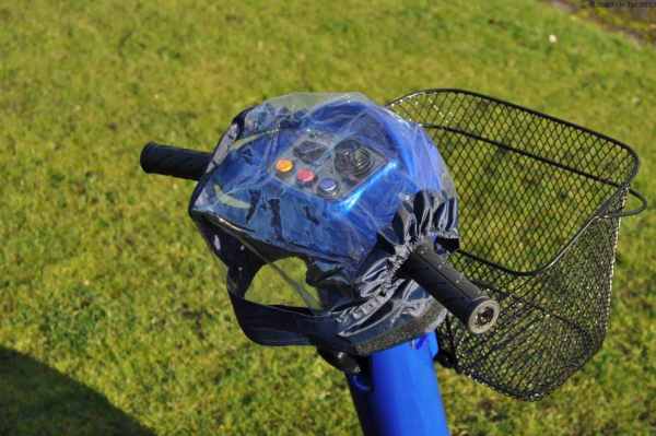 Electric mobility scooter handlebar with basket on grassy ground.
