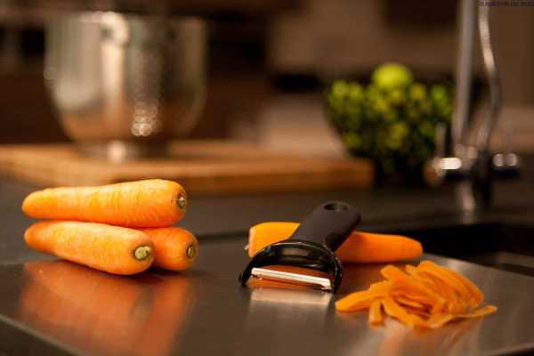 Fresh carrots and vegetable peeler on kitchen countertop, healthy cooking preparation.